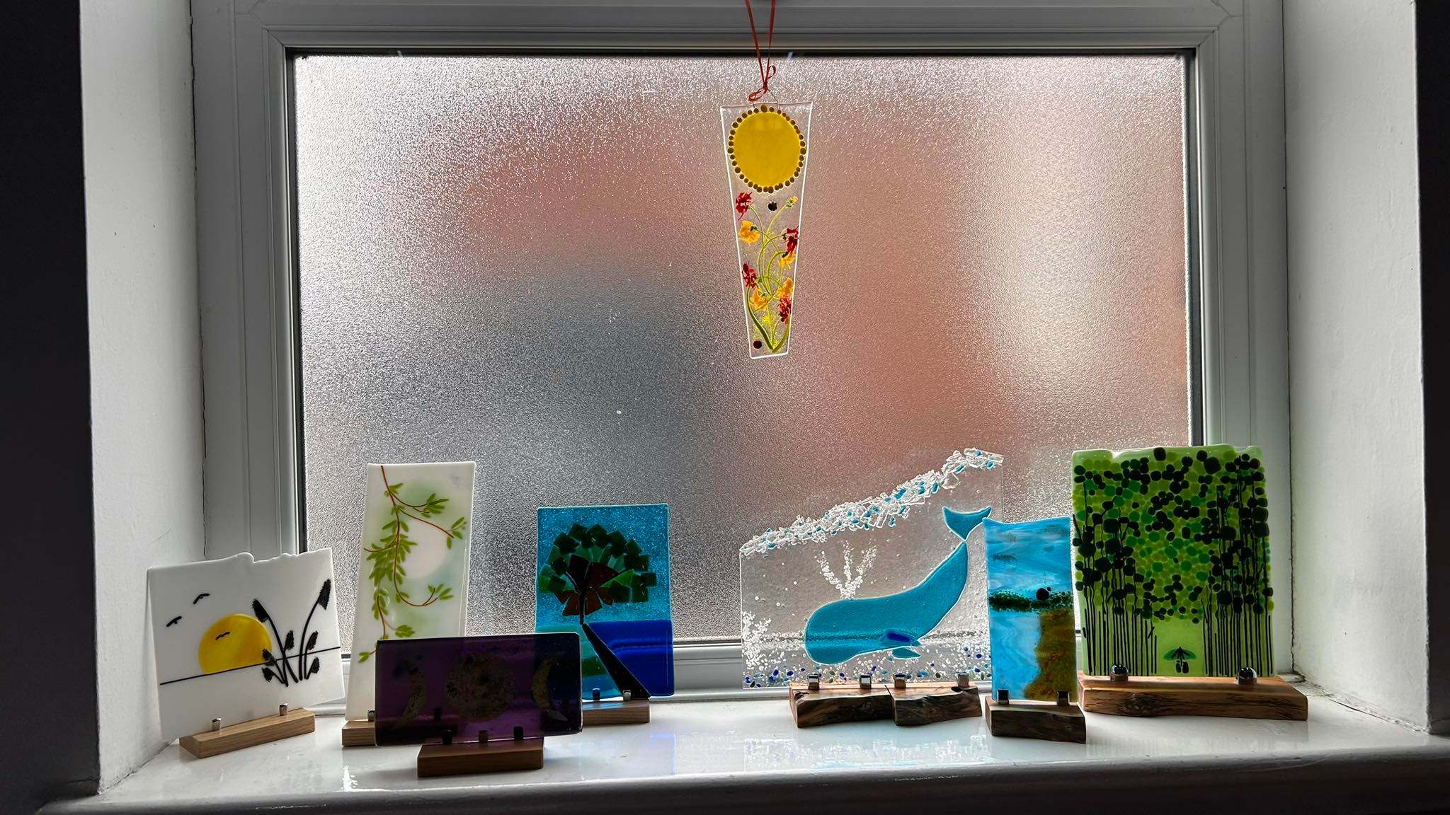 Studio windowsill display featuring collection of fused glass art